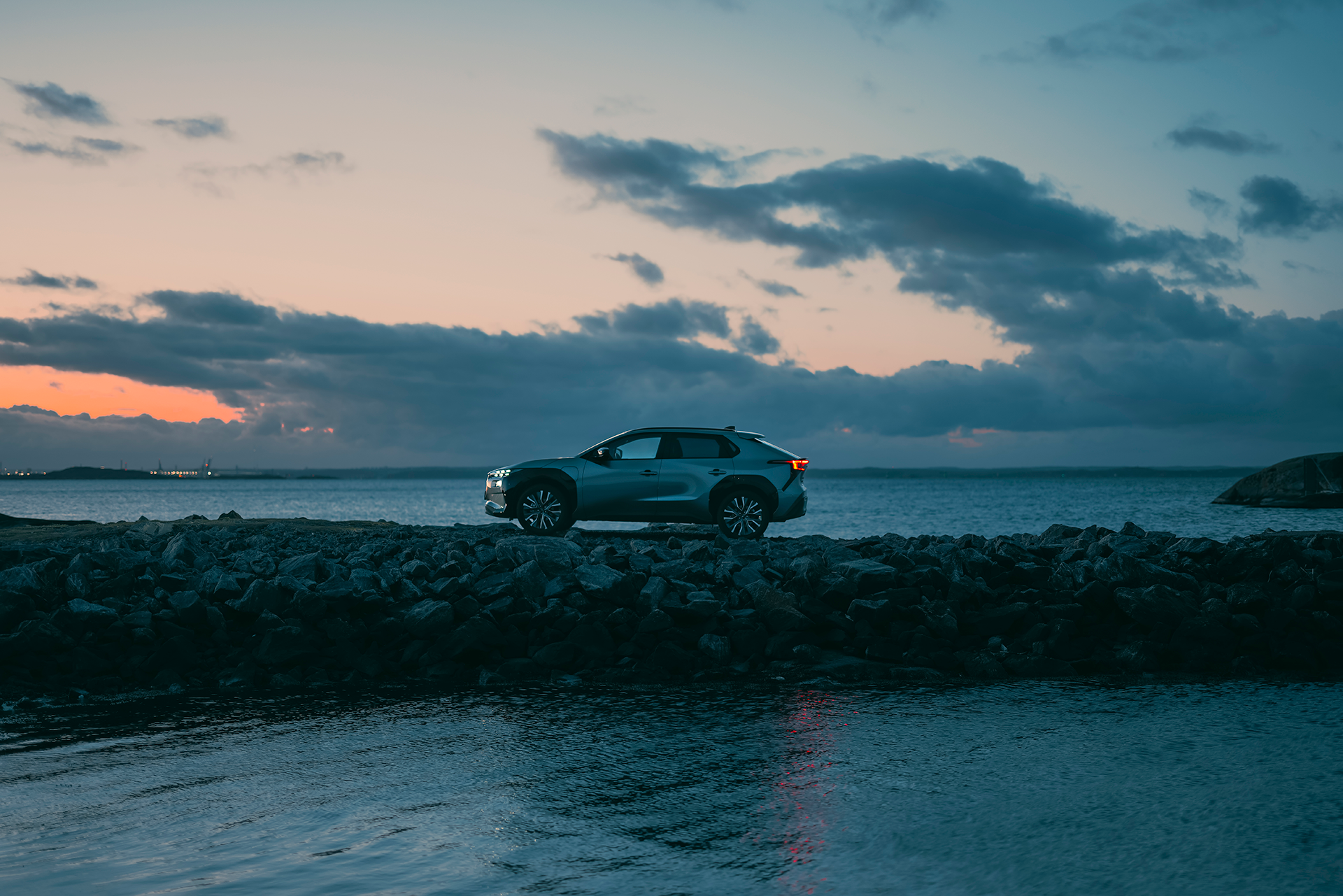 Subaru Solterra parkerad på en klippig kust vid havet i solnedgång.