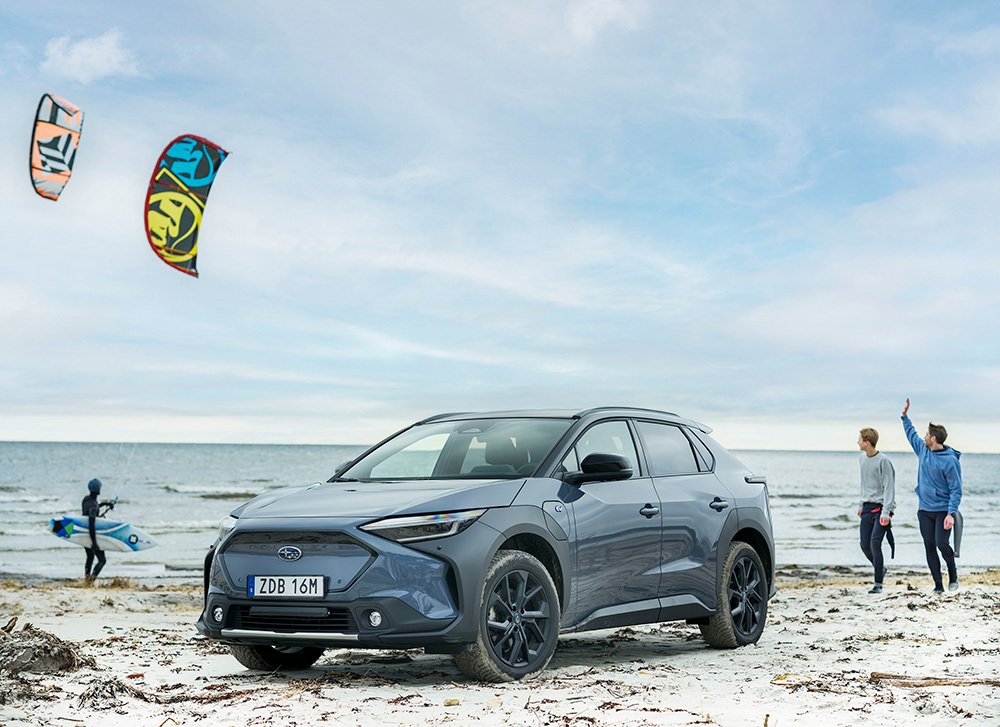 Subaru Solterra på en sandstrand med kitesurfare
